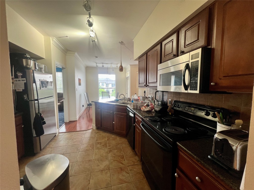 7701 Rialto Boulevard, Unit 1328 Austin, TX 78735 - Photo 6 of 17 Kitchen featuring black appliances, a peninsula, ornamental molding, decorative backsplash, and pendant lighting