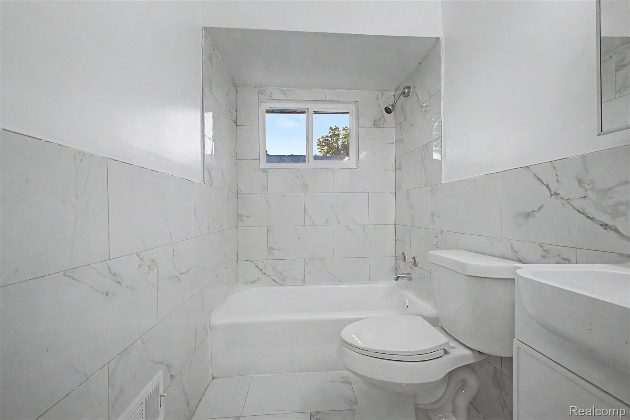 26718 Penn Street Inkster, MI 48141 - Photo 11 of 27 Bathroom featuring white tiled walls with subtle veining, a white bathtub, a toilet, a vanity with a white countertop, and a window providing natural light