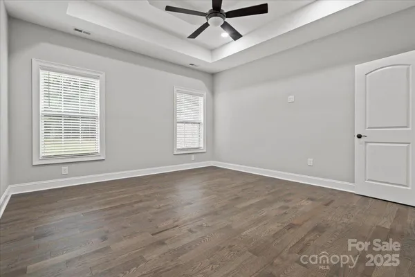 an empty room with wooden floor ceiling fan and windows
