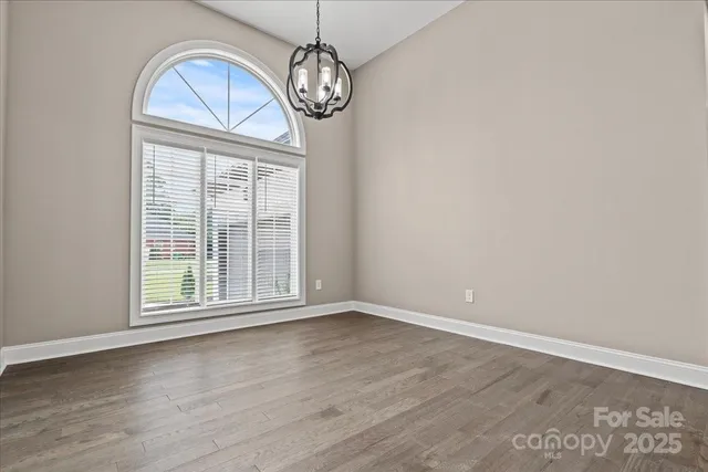 an empty room with wooden floor chandelier and windows