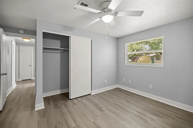 an empty room with wooden floor chandelier fan and windows