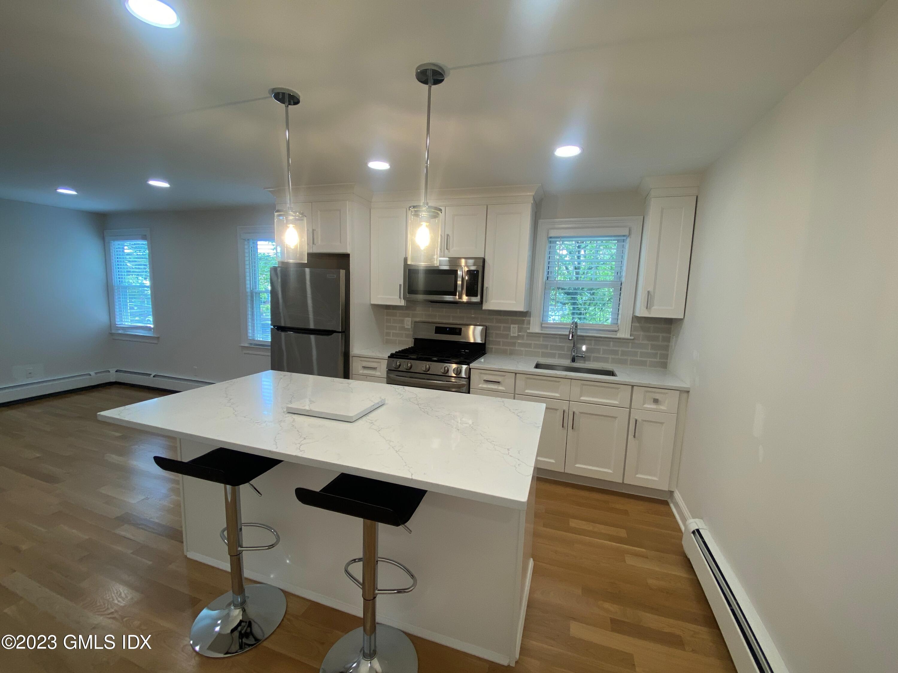 36 Arch Street, Unit 2A Greenwich, CT 06830 - Photo 2 of 9 a kitchen with stainless steel appliances kitchen island a stove a refrigerator a sink a dining table and chairs with wooden floor