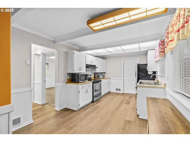 a living room with stainless steel appliances kitchen island granite countertop a refrigerator a stove a sink dishwasher and white cabinets with wooden floor