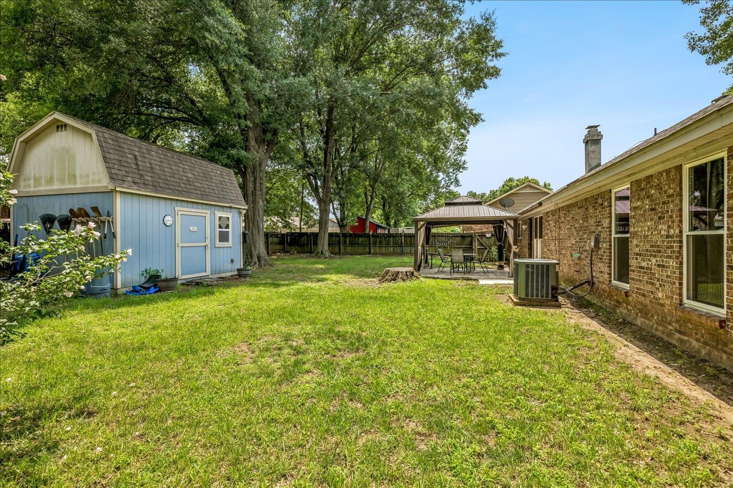 3284 Altruria Road Bartlett, TN 38134 - Photo 28 of 28 Expansive green lawn featuring a blue storage shed, mature trees, and a covered patio area with a gazebo