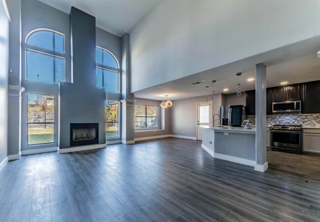924 Satellite View Round Rock, TX 78665 - Photo 4 of 30 Unfurnished living room featuring crown molding, a fireplace, grey lvp finished floors, and a high ceiling