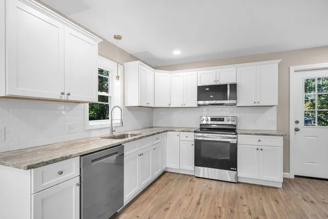 a kitchen with stainless steel appliances granite countertop a sink a stove top oven and white cabinets