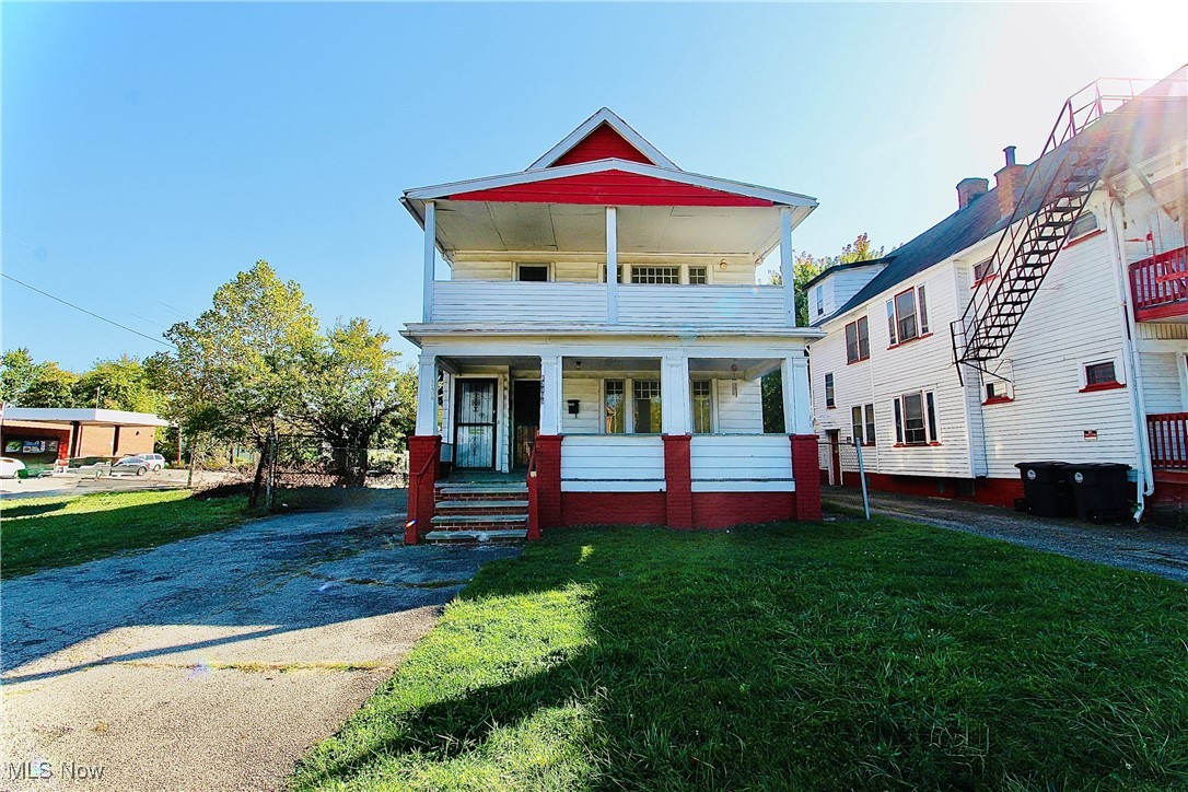 View of front of home featuring a front lawn, a balcony, driveway, and covered porch