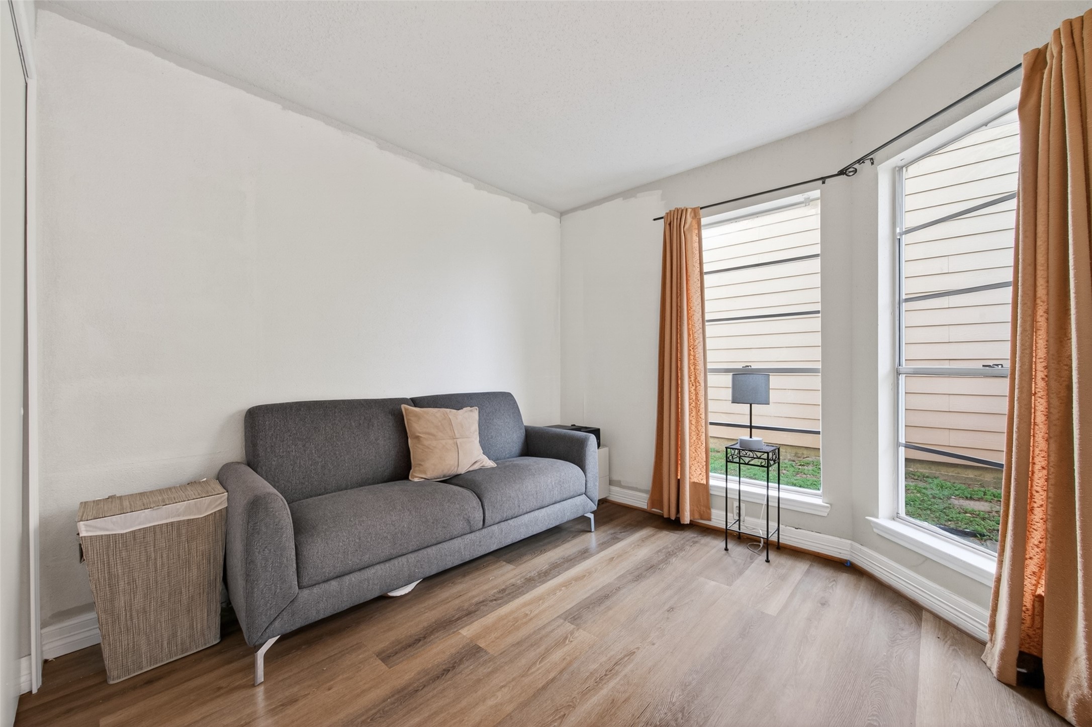 18446 North Willow Bluff Road Katy, TX 77449 - Photo 24 of 33 This cozy room features a modern gray sofa with a decorative pillow, hardwood flooring, and ample natural light from large windows with orange curtains. It's a bright and inviting space perfect for relaxation.