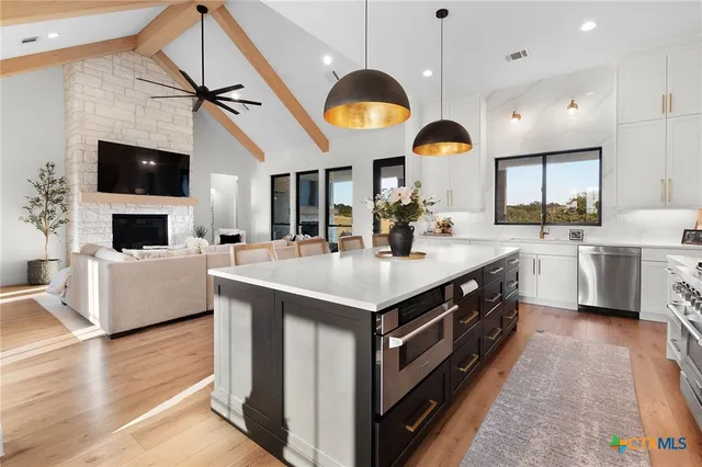 a spacious kitchen with stainless steel appliances granite countertop a white cabinets a sink a stove and a wooden floors