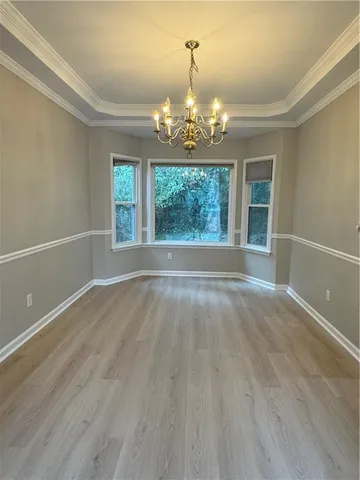 an empty room with wooden floor chandelier and windows