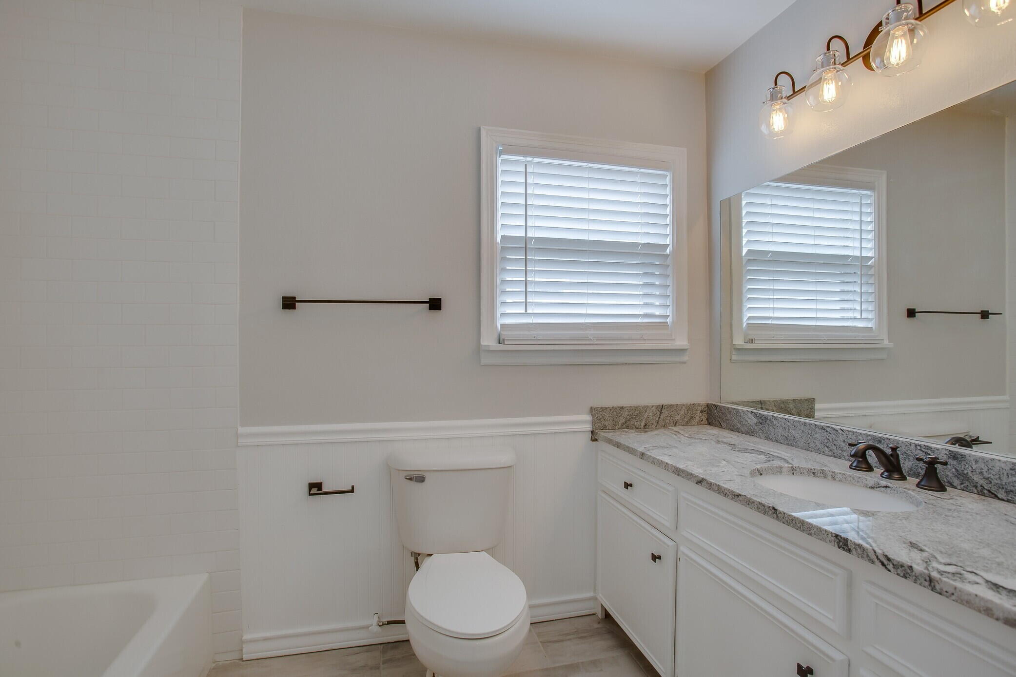3409 29th Street Lubbock, TX 79410 - Photo 13 of 16 a bathroom with a granite countertop sink toilet a large mirror and a bathtub