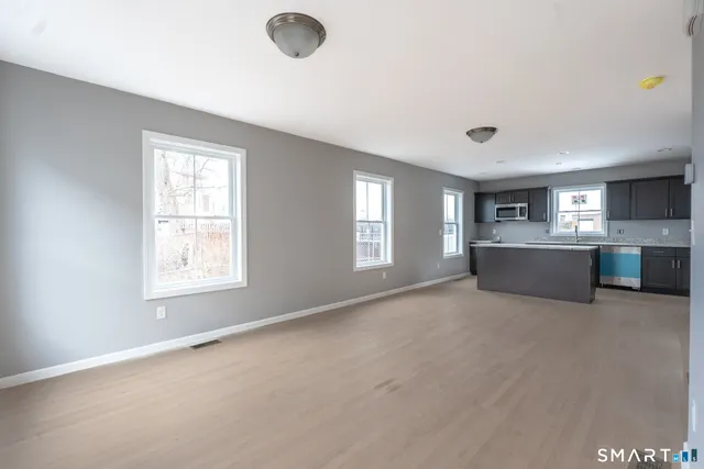 a view of an empty room with a window and kitchen view