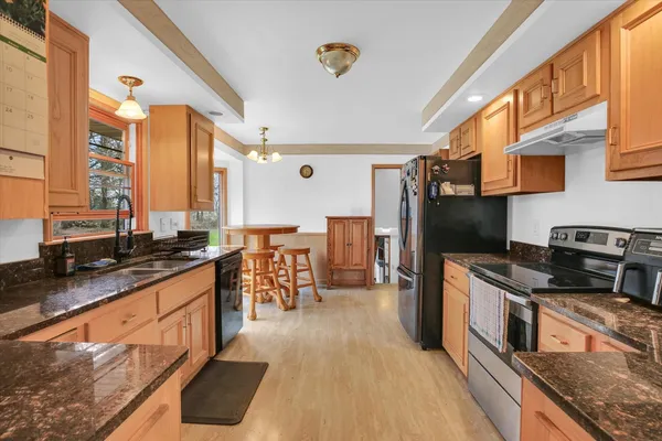 a kitchen with stainless steel appliances granite countertop a refrigerator a sink dishwasher a stove and white countertops with wooden floor