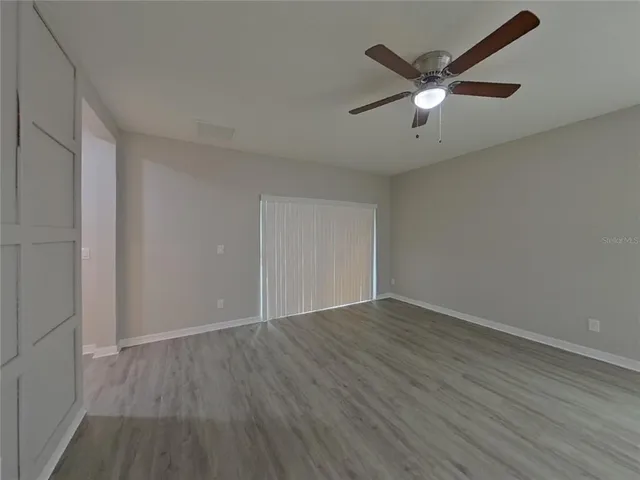 an empty room with wooden floor fan and windows