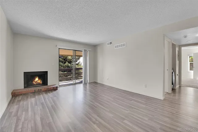 a view of an empty room with wooden floor fireplace and a window