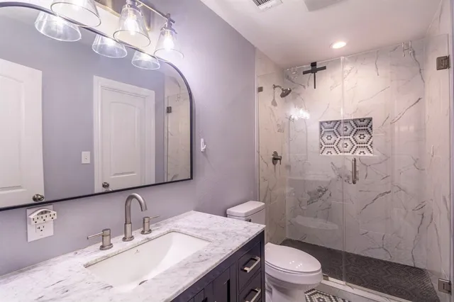 a bathroom with a granite countertop sink toilet a mirror a vanity and shower