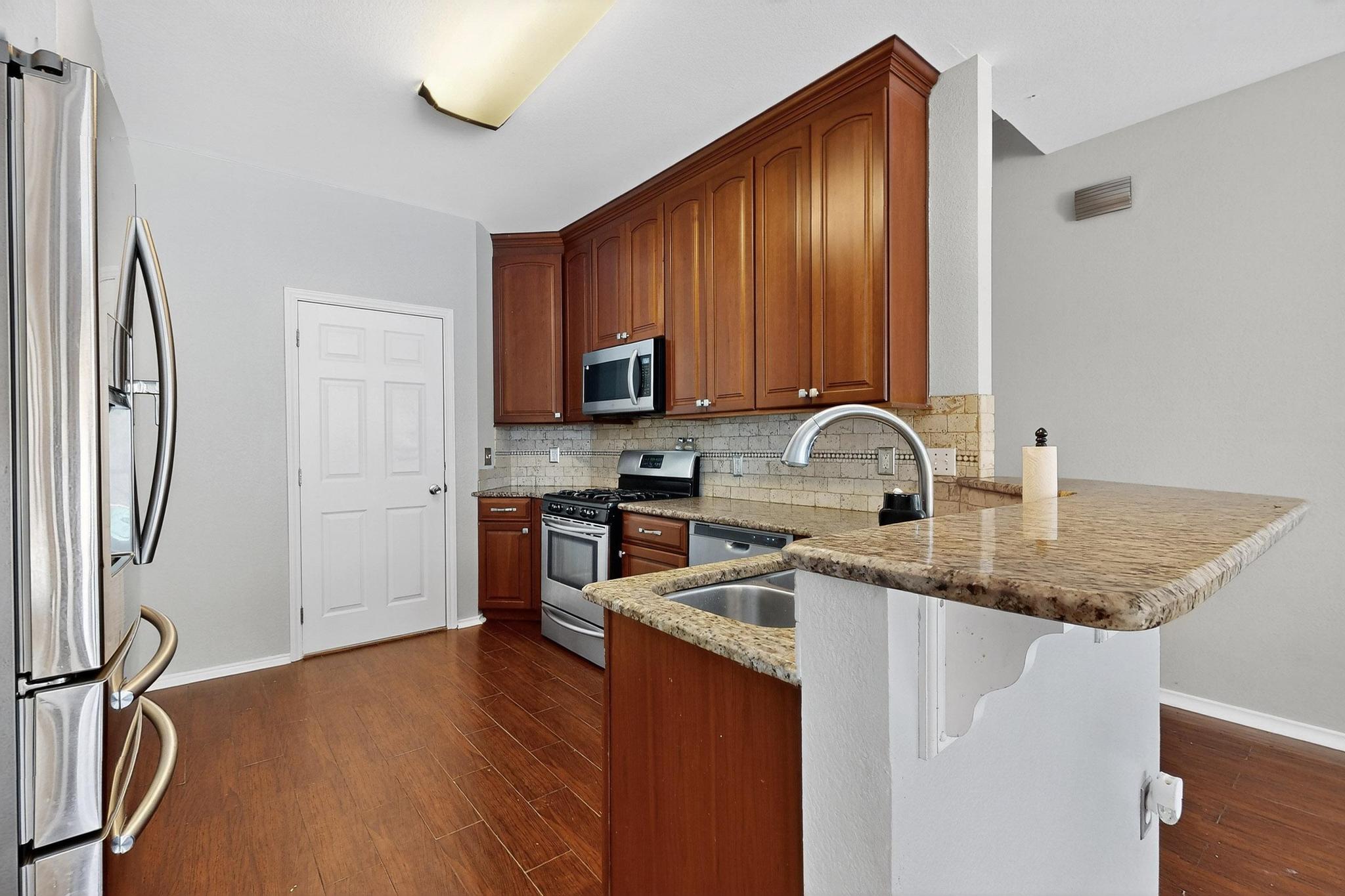 2403 Willow Way Round Rock, TX 78664 - Photo 15 of 35 Kitchen with stainless steel appliances, a peninsula, light stone counters, tasteful backsplash, and dark wood-type flooring