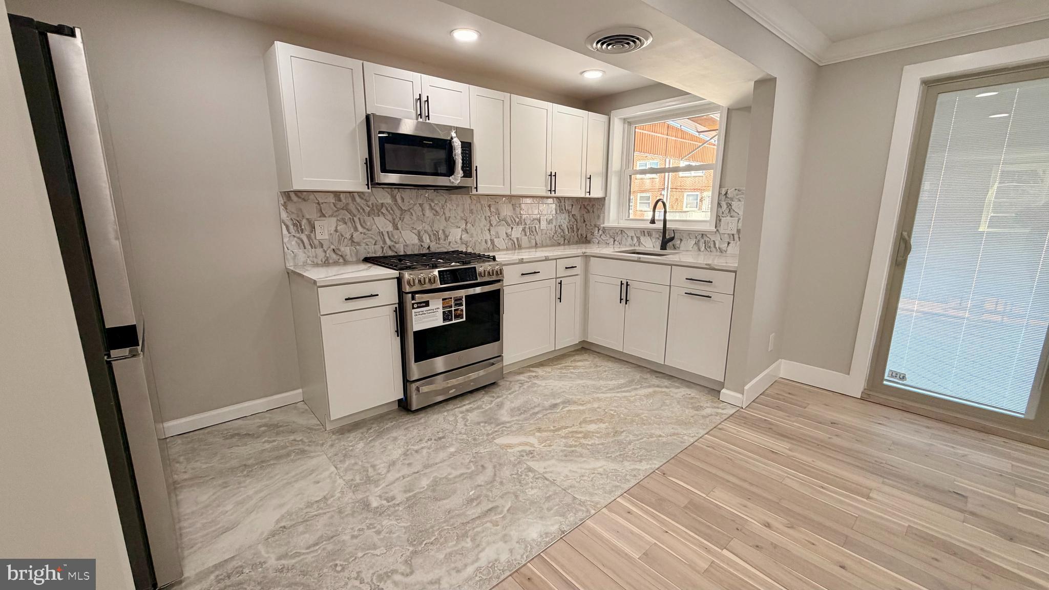 7219 Saul Street Philadelphia, PA 19149 - Photo 6 of 24 a kitchen with granite countertop a stove top oven a sink and a microwave
