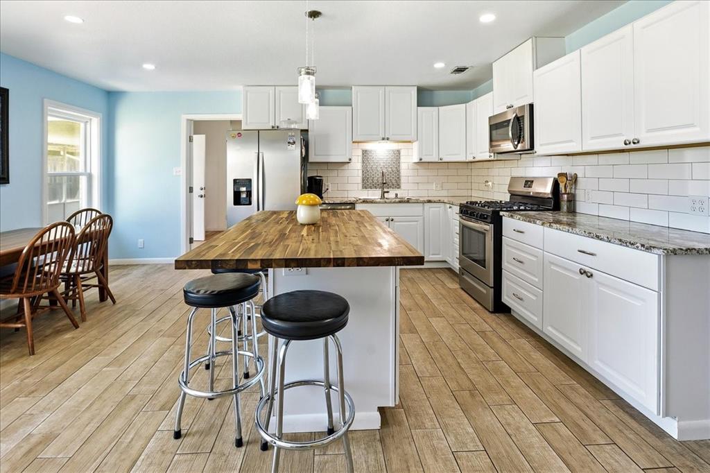 12657 Alma Street Tyler, TX 75704 - Photo 6 of 36 a kitchen with stainless steel appliances granite countertop a stove a refrigerator a sink a dining table and chairs with wooden floor