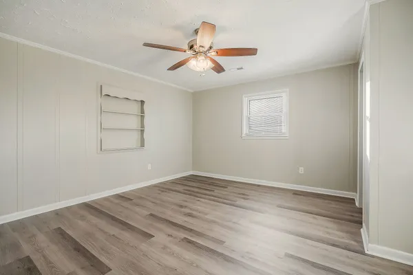 an empty room with wooden floor ceiling fan and windows