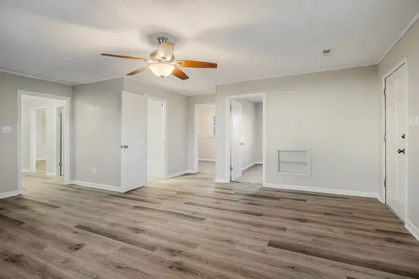 a view of an empty room with wooden floor and a ceiling fan