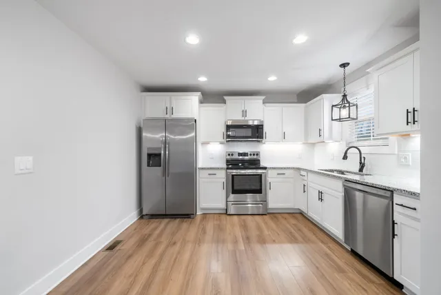 a kitchen with stainless steel appliances a sink dishwasher a refrigerator and a stove top oven with wooden floor