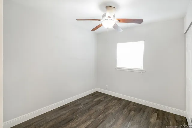 an empty room with wooden floor fan and window