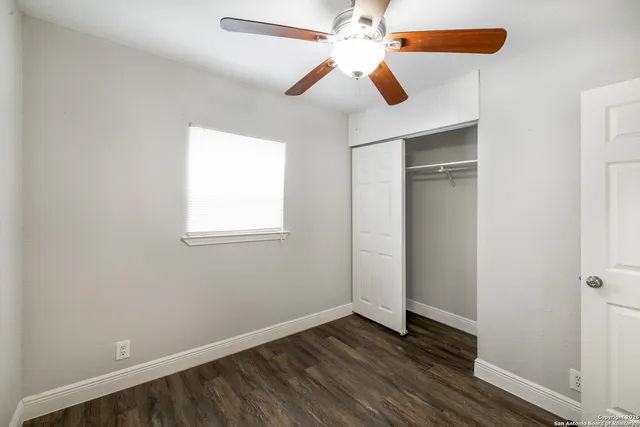 an empty room with wooden floor fan and windows