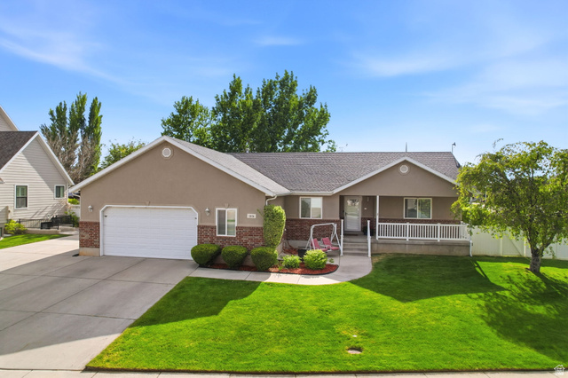 1816 River Bottom Road Springville, UT 84663 - Photo 2 of 37 Ranch-style exterior featuring a stucco and brick facade, an attached garage, a covered front porch with white railing, a concrete driveway, and a manicured front lawn