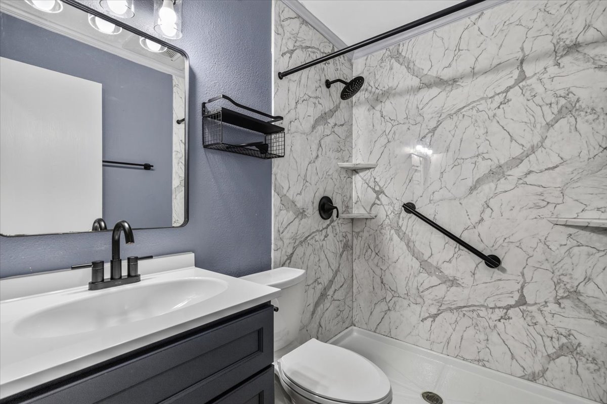 6200 Shadow Bend Austin, TX 78745 - Photo 17 of 33 Modern bathroom featuring a stylish vanity with a contrasting cabinet and a spacious shower with sleek, marbled wall panels.