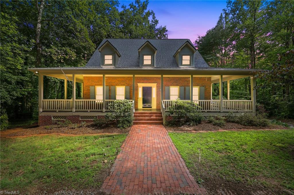 8861 Boylston Road Colfax, NC 27235 - Photo 1 of 50 A timeless Cape Cod estate where classic architecture, a full wraparound porch, and a peaceful wooded setting create exceptional curb appeal (Enhanced Twilight Front Elevation)