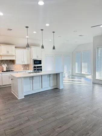 a large kitchen with granite countertop a stove top oven a sink and white cabinets with wooden floor