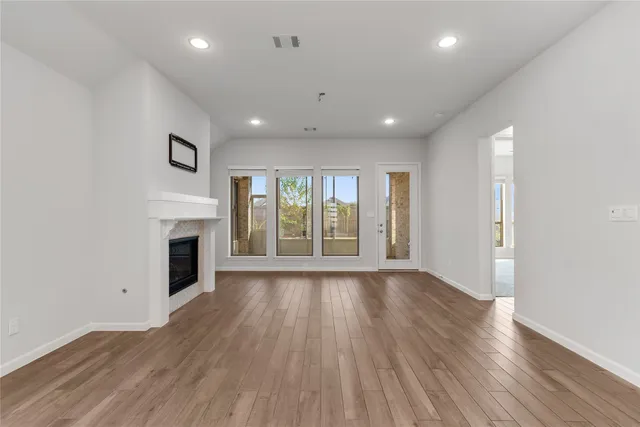 a view of an empty room with wooden floor and a kitchen