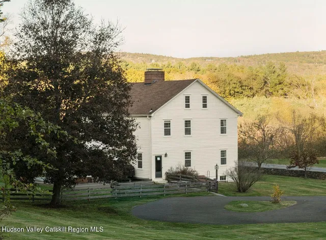 a view of a white house next to a yard with big trees