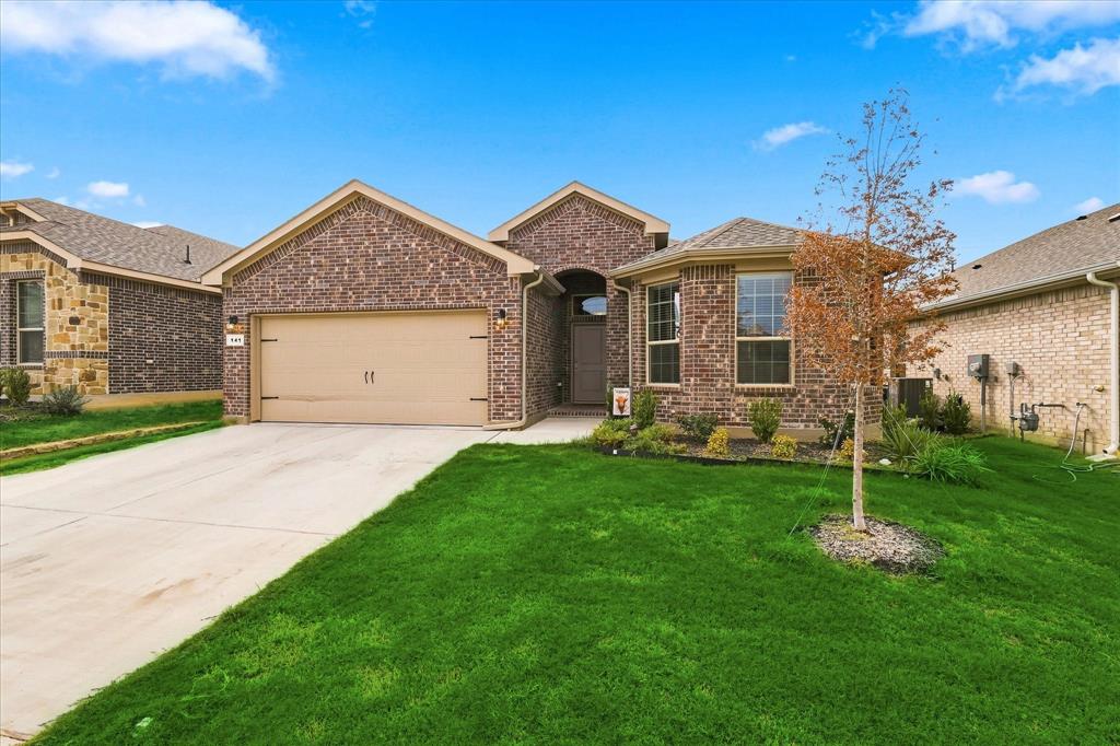 Brick exterior, two-car garage, concrete driveway, landscaped front yard, and a mature tree