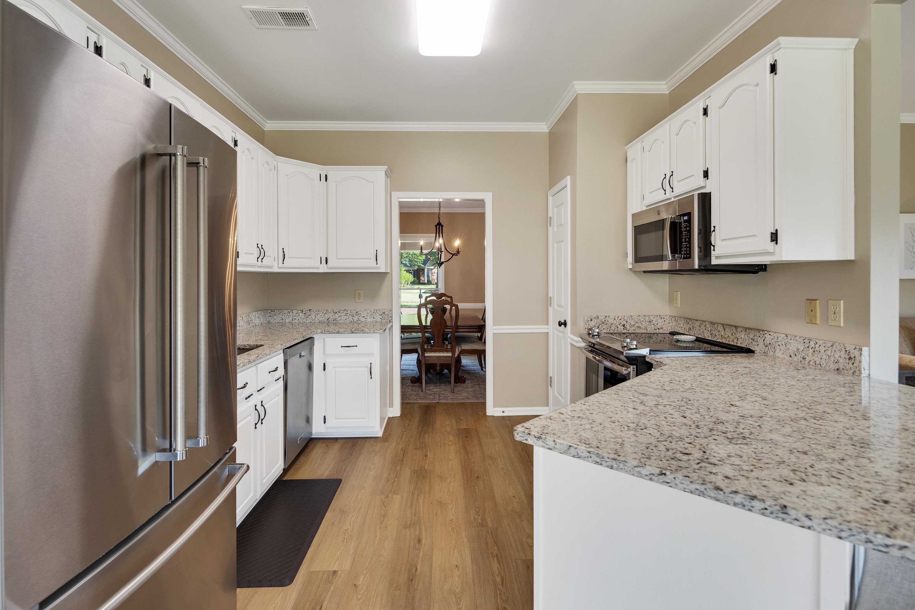 540 Whitney Way Collierville, TN 38017 - Photo 9 of 22 Kitchen with stainless steel appliances, ornamental molding, light stone countertops, white cabinets, and light wood-type flooring