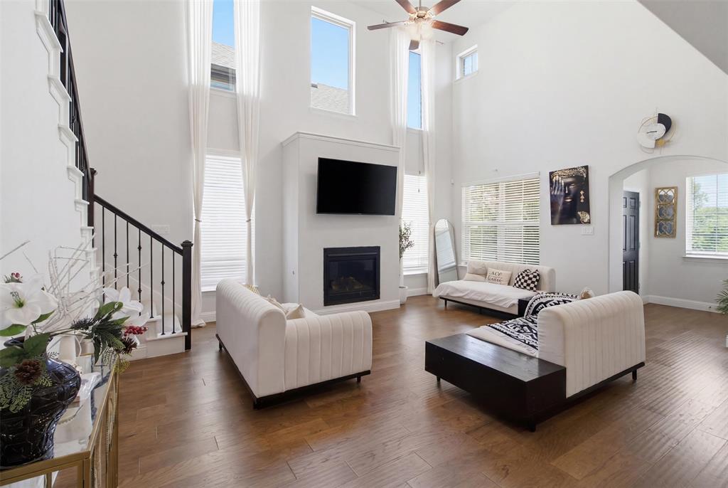 7416 Sequoia Rdg Road Little Elm, TX 76227 - Photo 13 of 37 Vaulted living area featuring wood-finish flooring, a contemporary fireplace with a mounted television, and a visible staircase with wrought iron balusters