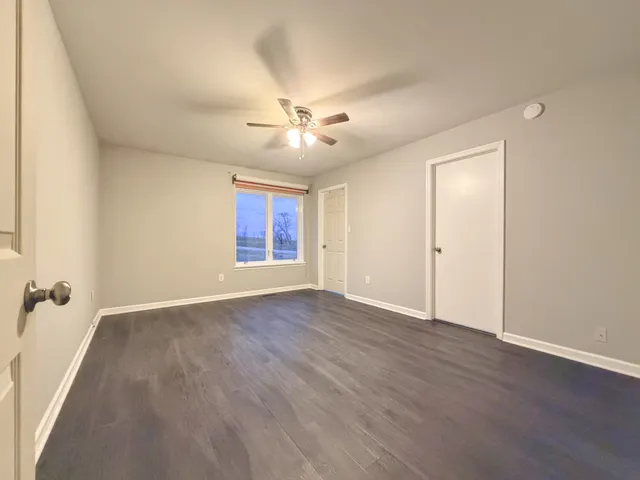 an empty room with wooden floor ceiling fan and windows