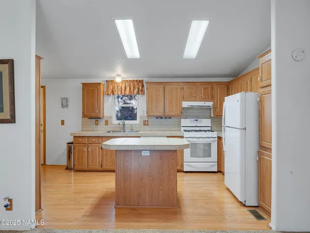 a kitchen with stainless steel appliances granite countertop a refrigerator a sink dishwasher a stove with wooden cabinets and wooden floor