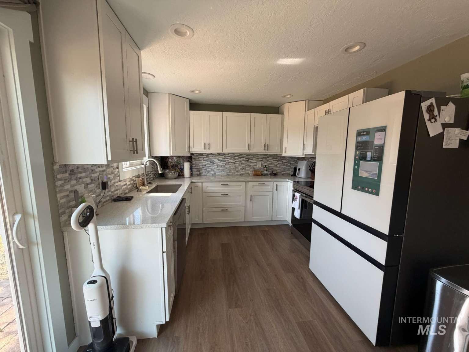 9951 West Fox Ridge Drive Boise, ID 83709 - Photo 10 of 13 Modern kitchen featuring white cabinetry, light stone-finish countertops, and a patterned tile backsplash
