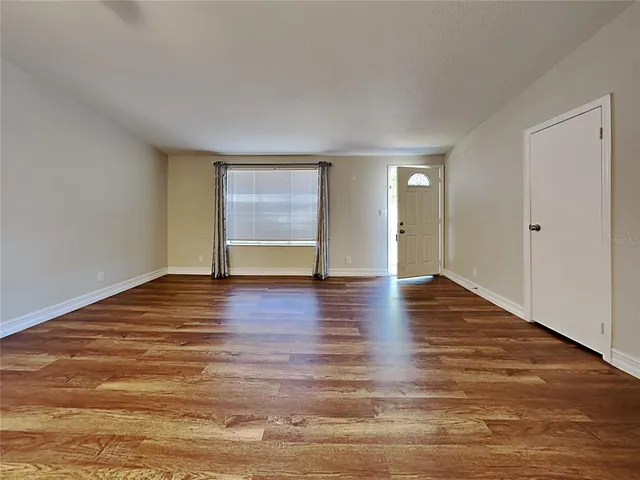 a view of an empty room with wooden floor and a window