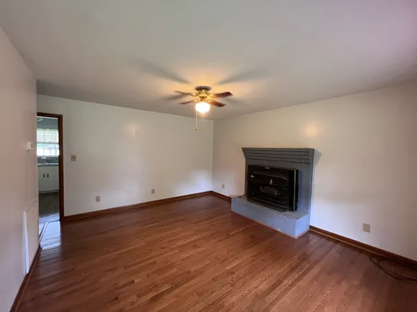 an empty room with wooden floor a chandelier fan and a fireplace