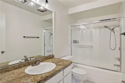 a bathroom with a sink granite countertop toilet a mirror and shower