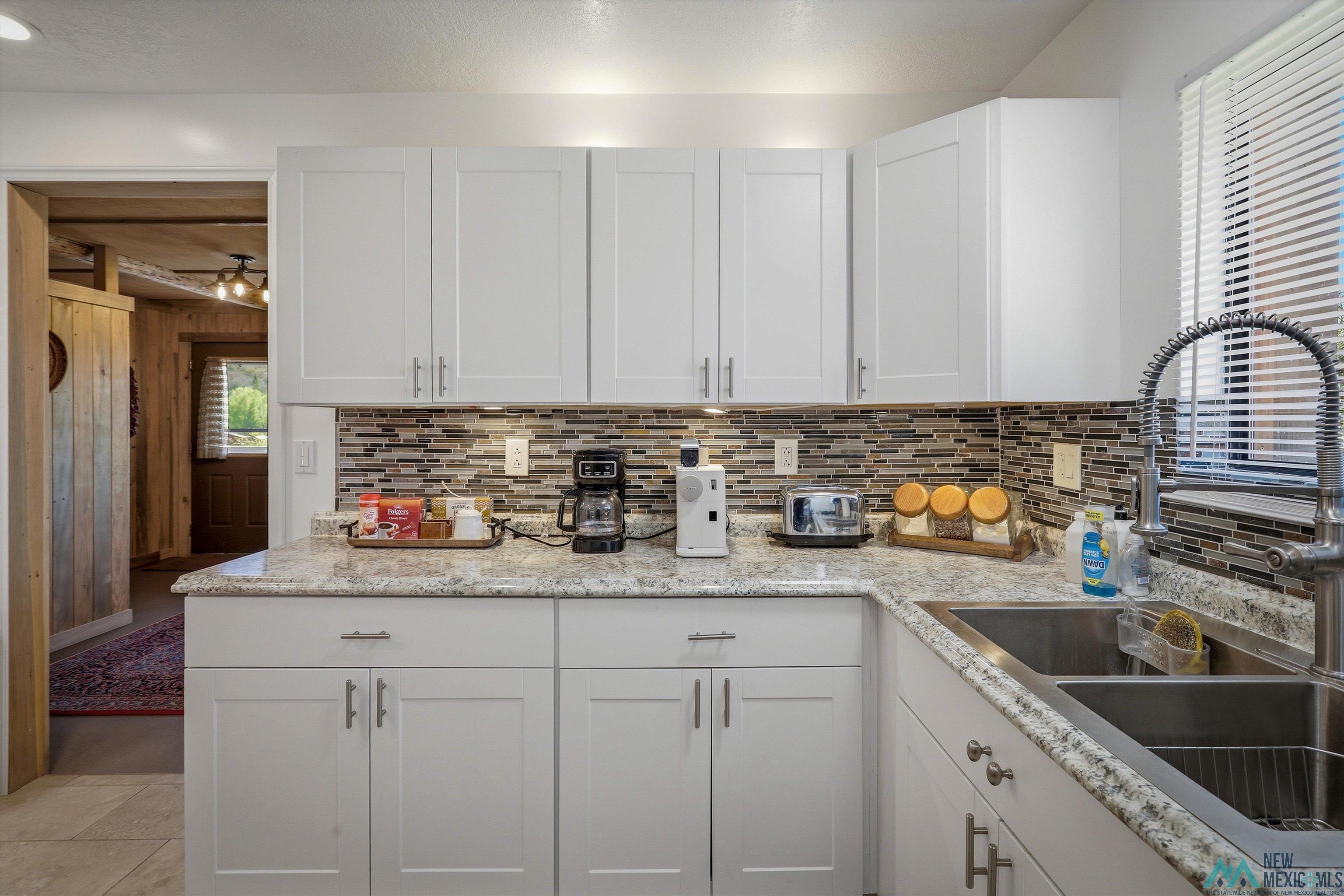 83 Juniper Road Chama, NM 87520 - Photo 11 of 56 Kitchen featuring white shaker-style cabinetry, a multi-tone tile backsplash, light-colored speckled countertops, and a dual-basin stainless steel sink with a gooseneck faucet