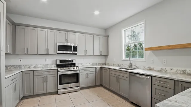 a kitchen with white cabinets appliances a sink and a window