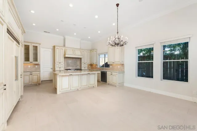 a large white kitchen with granite countertop a stove top oven a sink a refrigerator and a dining table