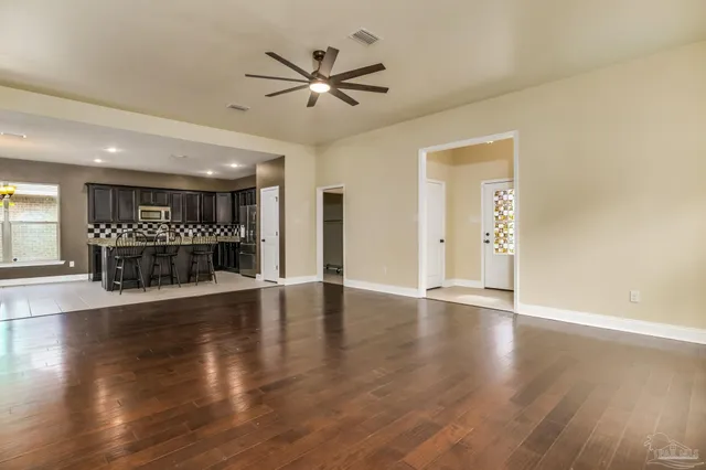 a view of an empty room with wooden floor and a ceiling fan