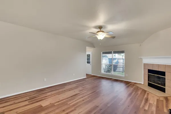 an empty room with wooden floor fireplace and windows