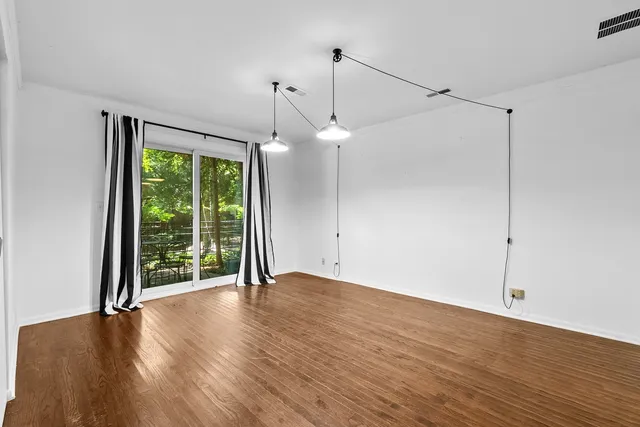 a view of an empty room with wooden floor fridge and a window