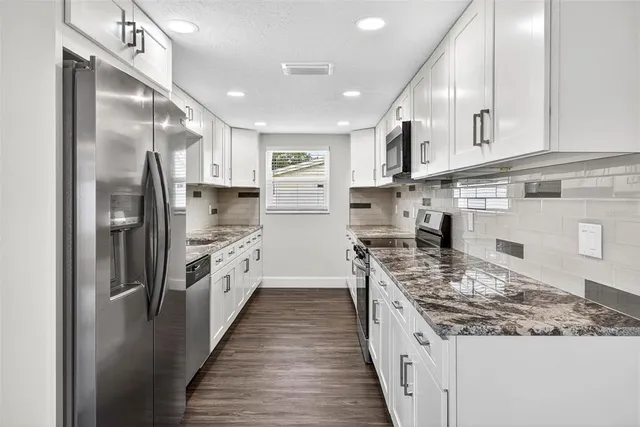 a large kitchen with stainless steel appliances kitchen island a large counter top and wooden cabinets